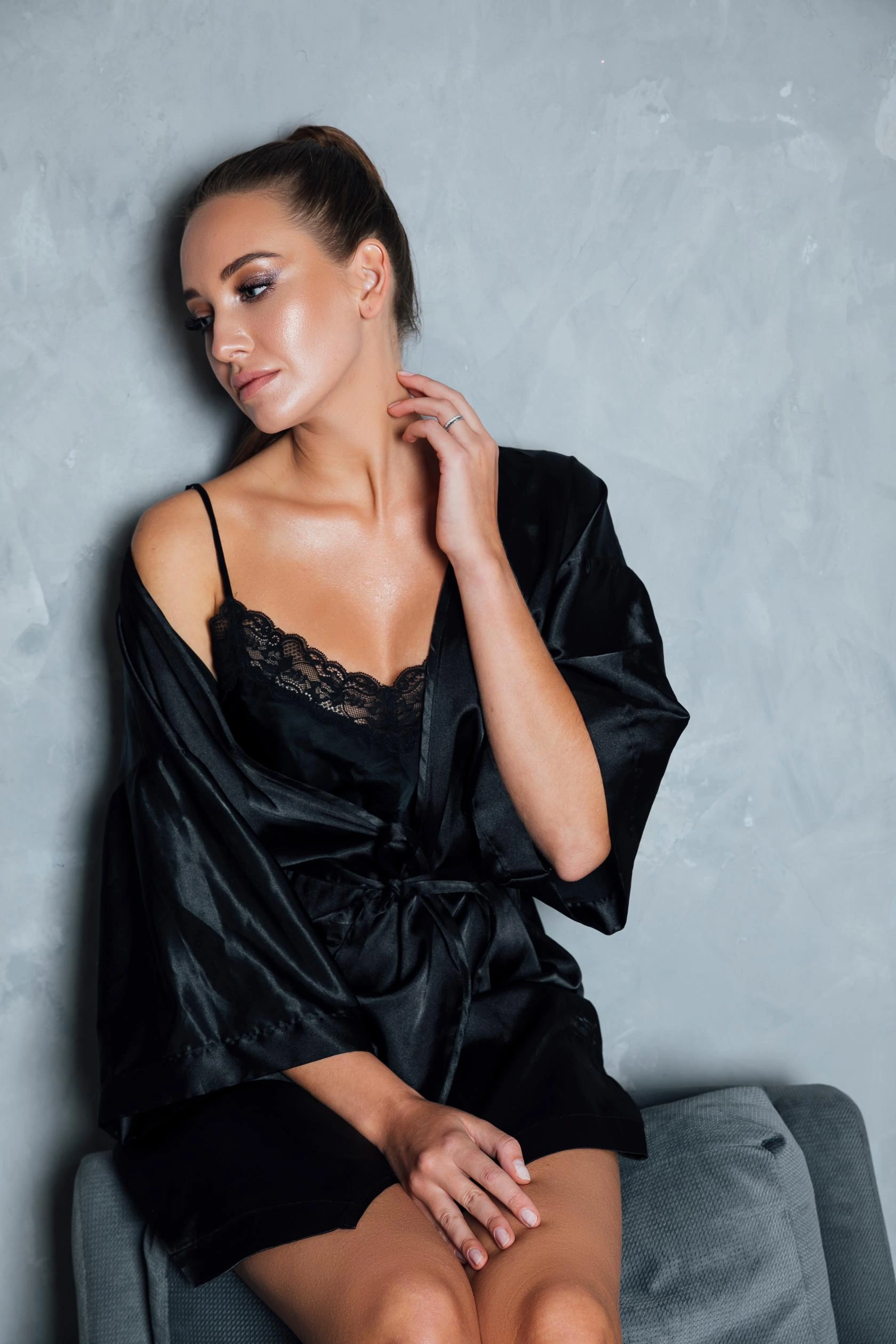 Woman in a black lace-trimmed nightgown and robe sitting on a chair, touching her neck.