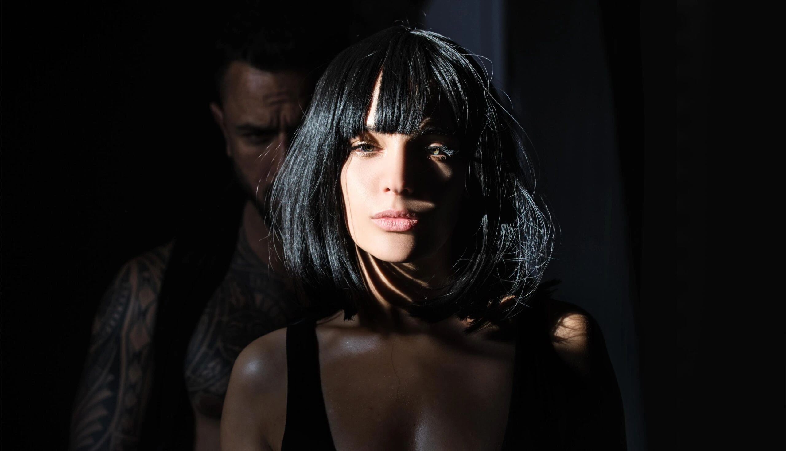 Woman with sharp black bob under spotlight, mystery and defiance