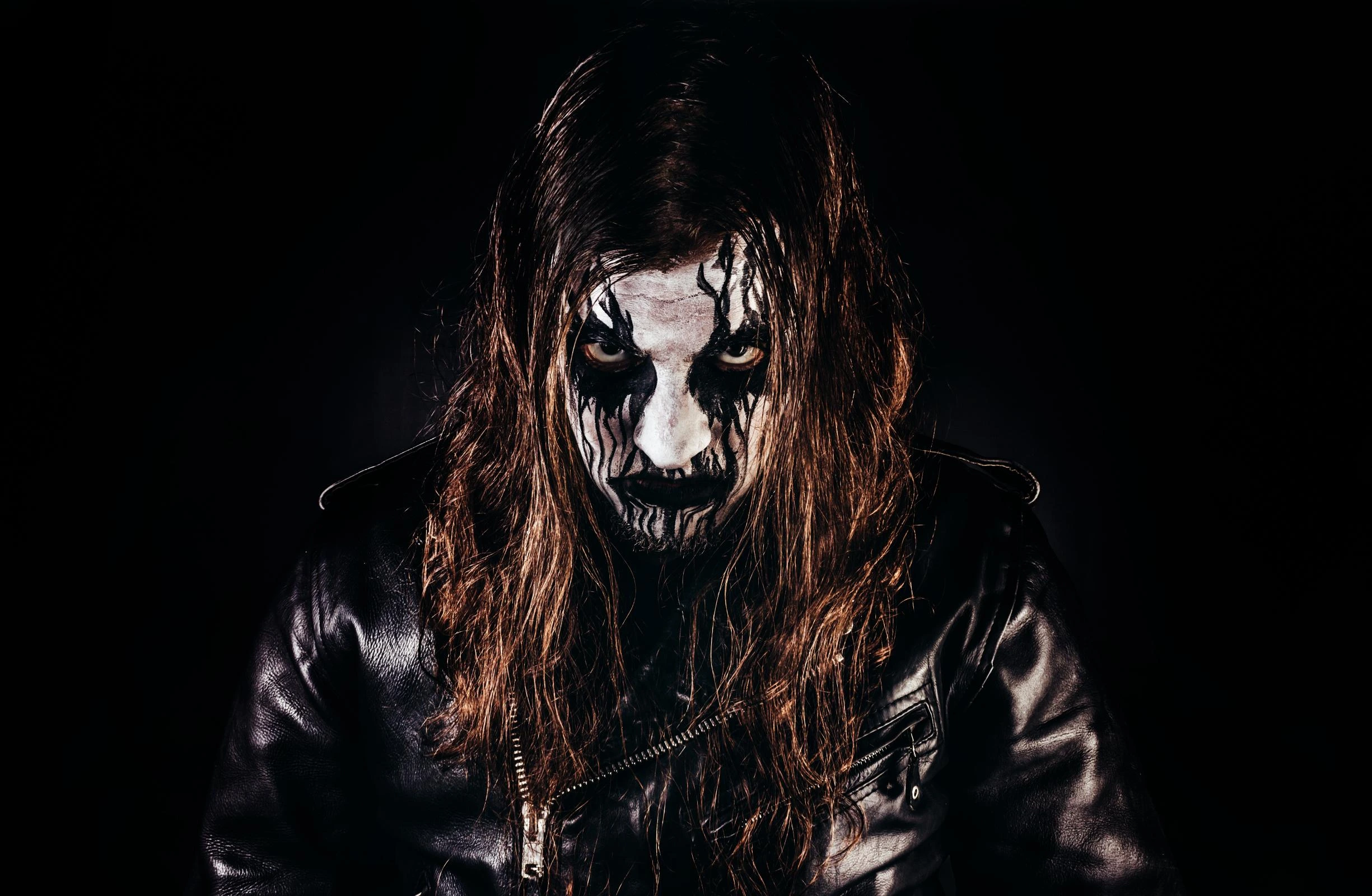 Black metal musician with corpse paint and leather, grim and intense stare