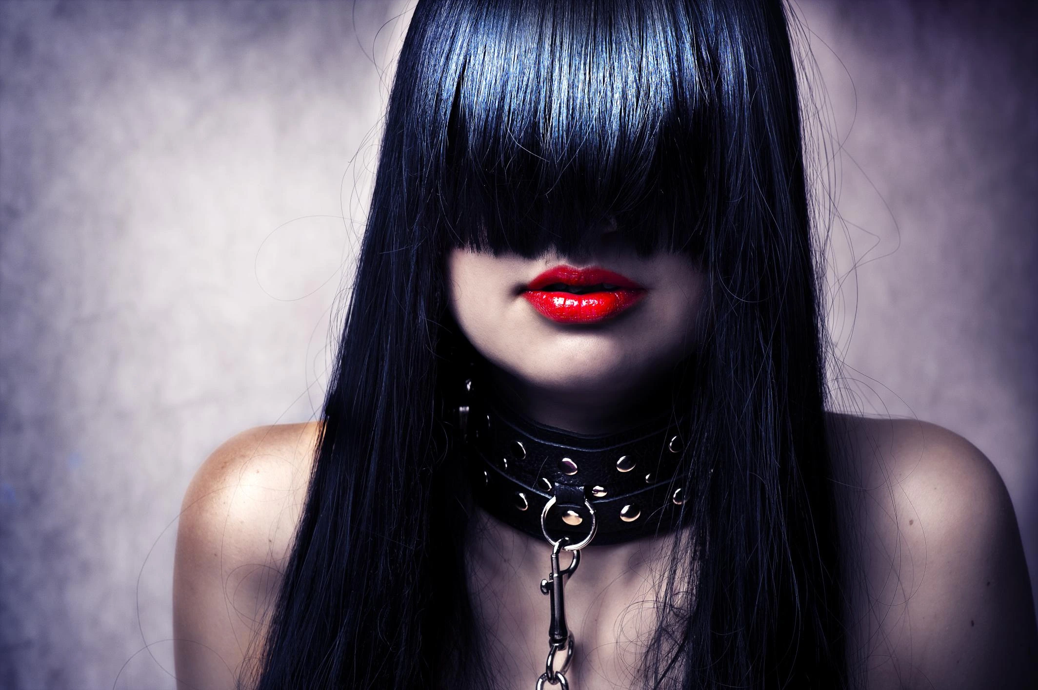 Woman with long black hair covering eyes, wearing red lipstick and a studded leather collar with leash