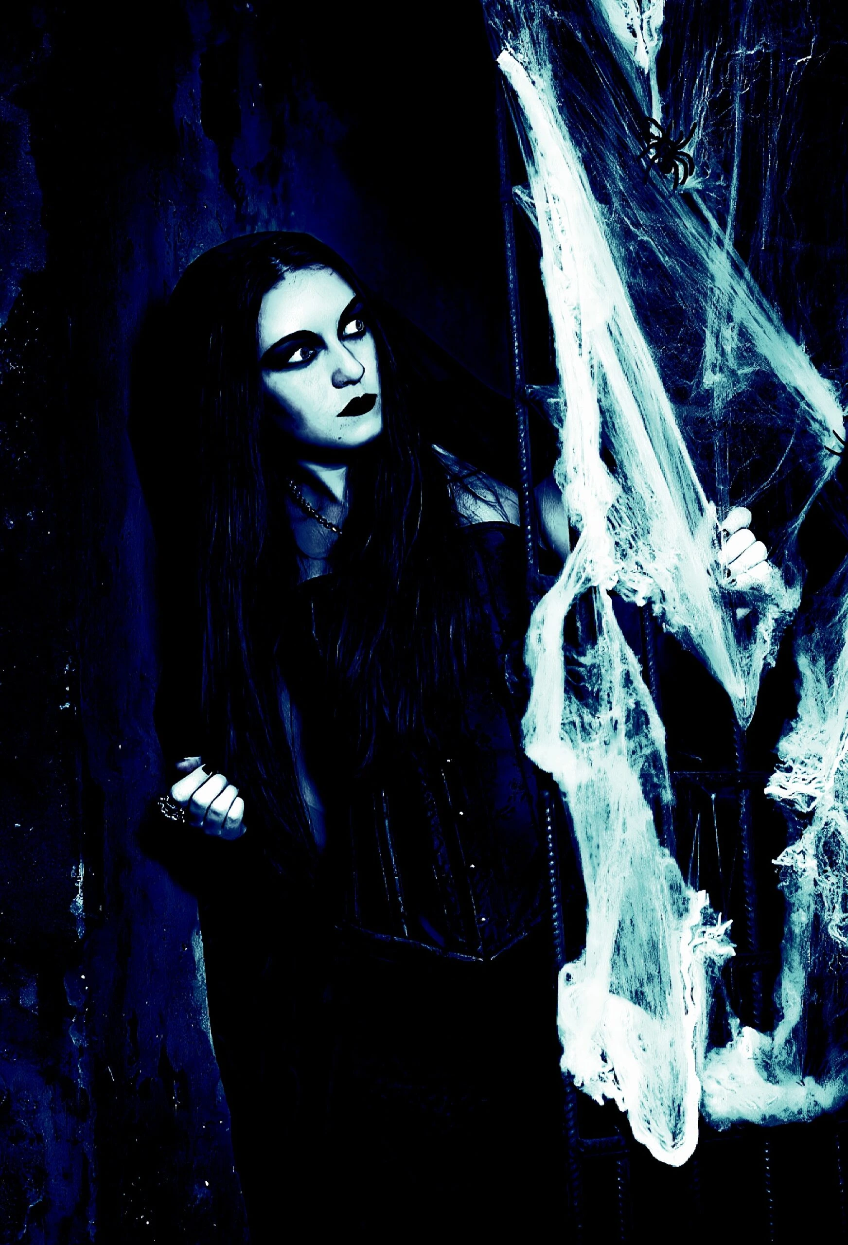 Gothic woman in black corset peering through cobwebs in a spooky, dark setting with heavy shadows.