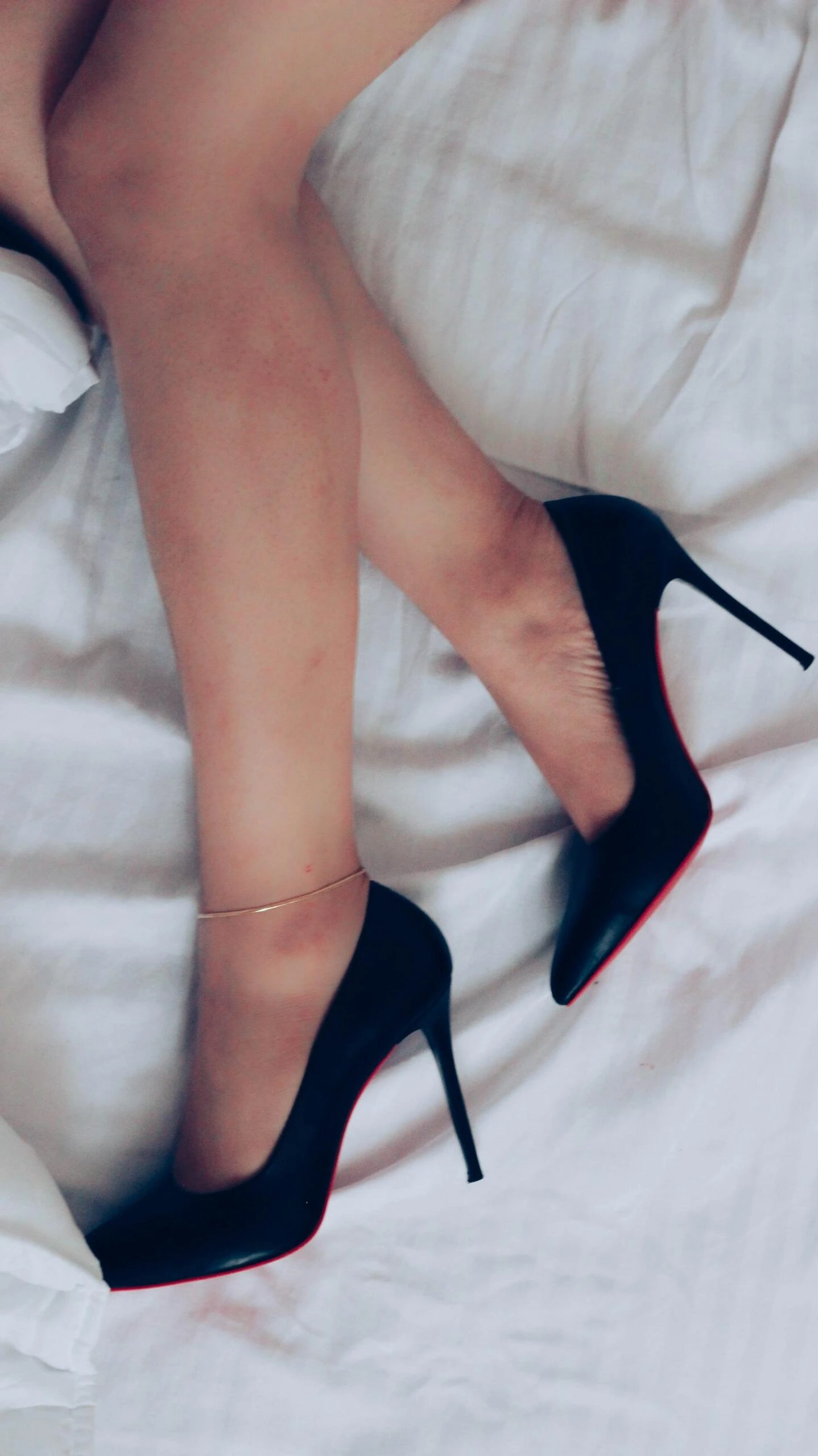 Close-up of legs in black stiletto women's high heel shoes on white sheets, exuding sensual elegance.