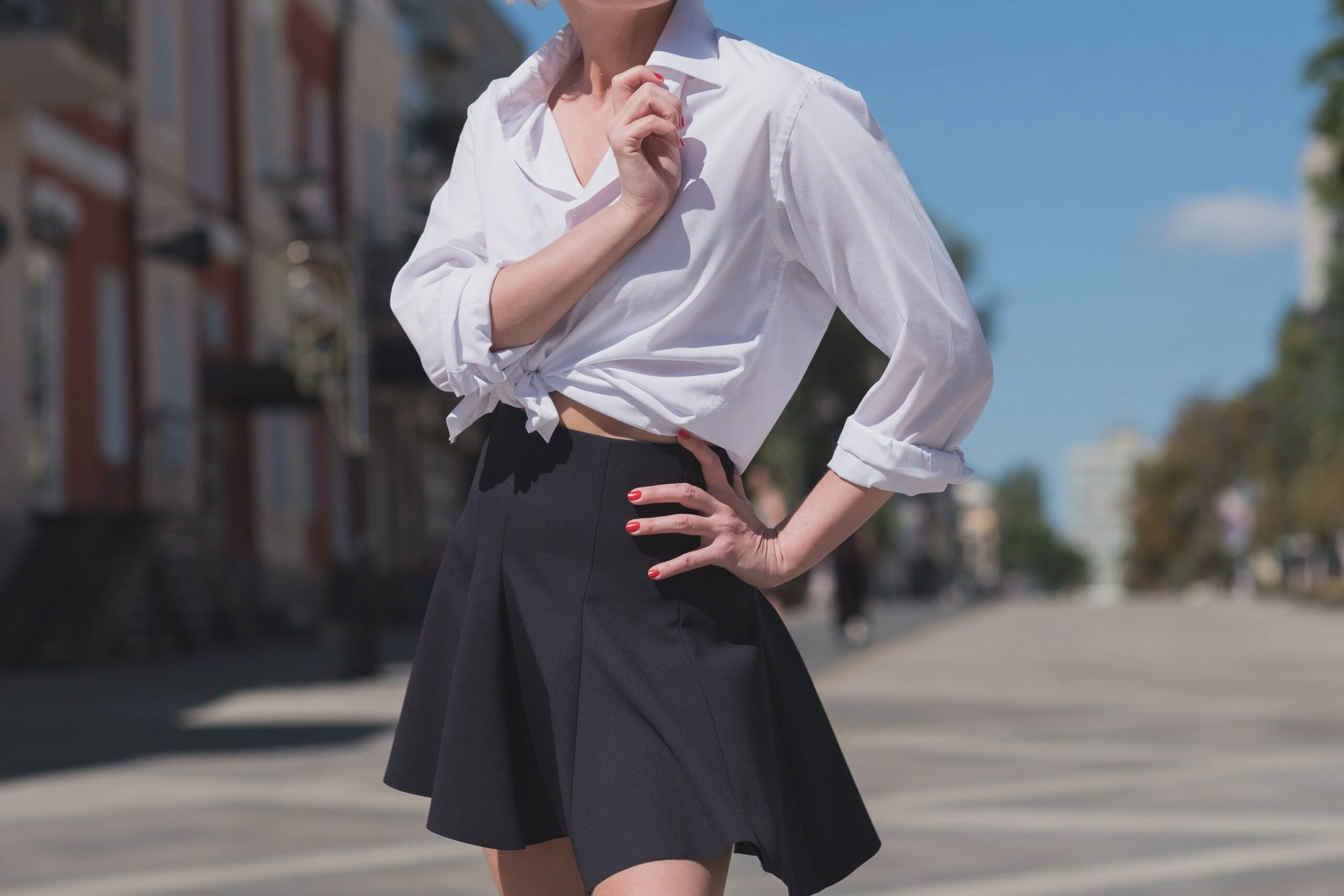 Woman in a black skater skirt and tied white shirt posing confidently in an urban setting