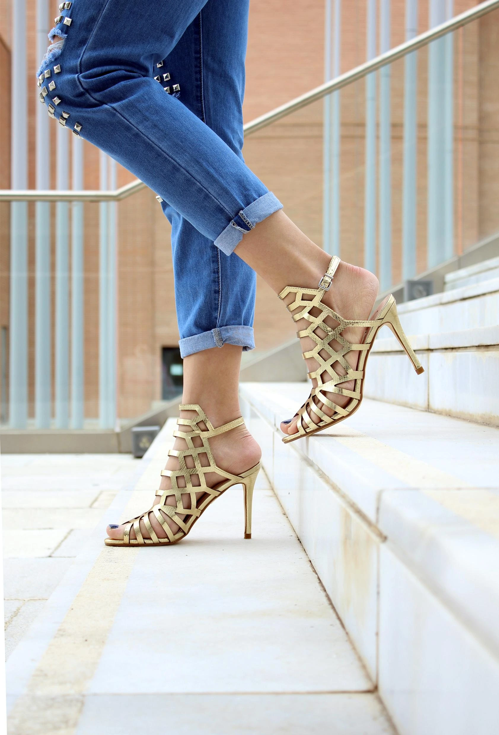 Woman stepping up stairs in golden cage women's high heel shoes, combining luxury and dominance.