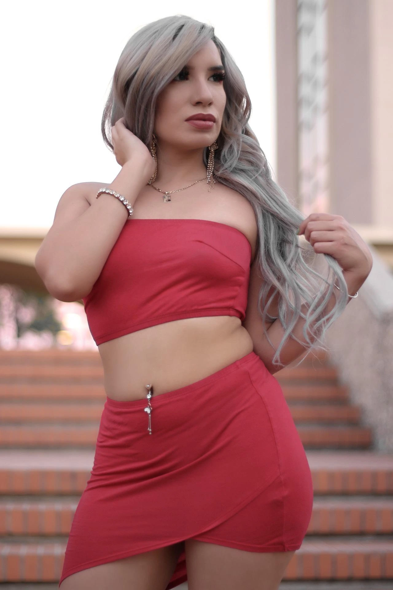 Woman in a red asymmetrical mini skirt set with silver jewelry and long gray-blonde hair