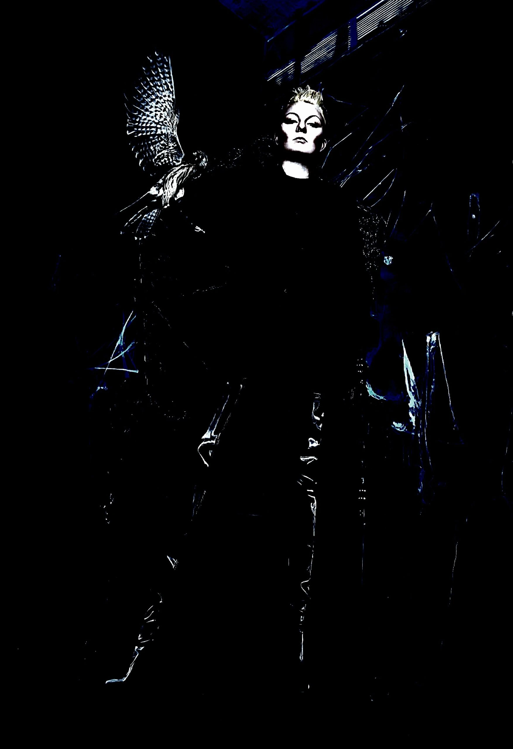  Dark gothic figure in black leather with feather details, posing in a shadowy scene.