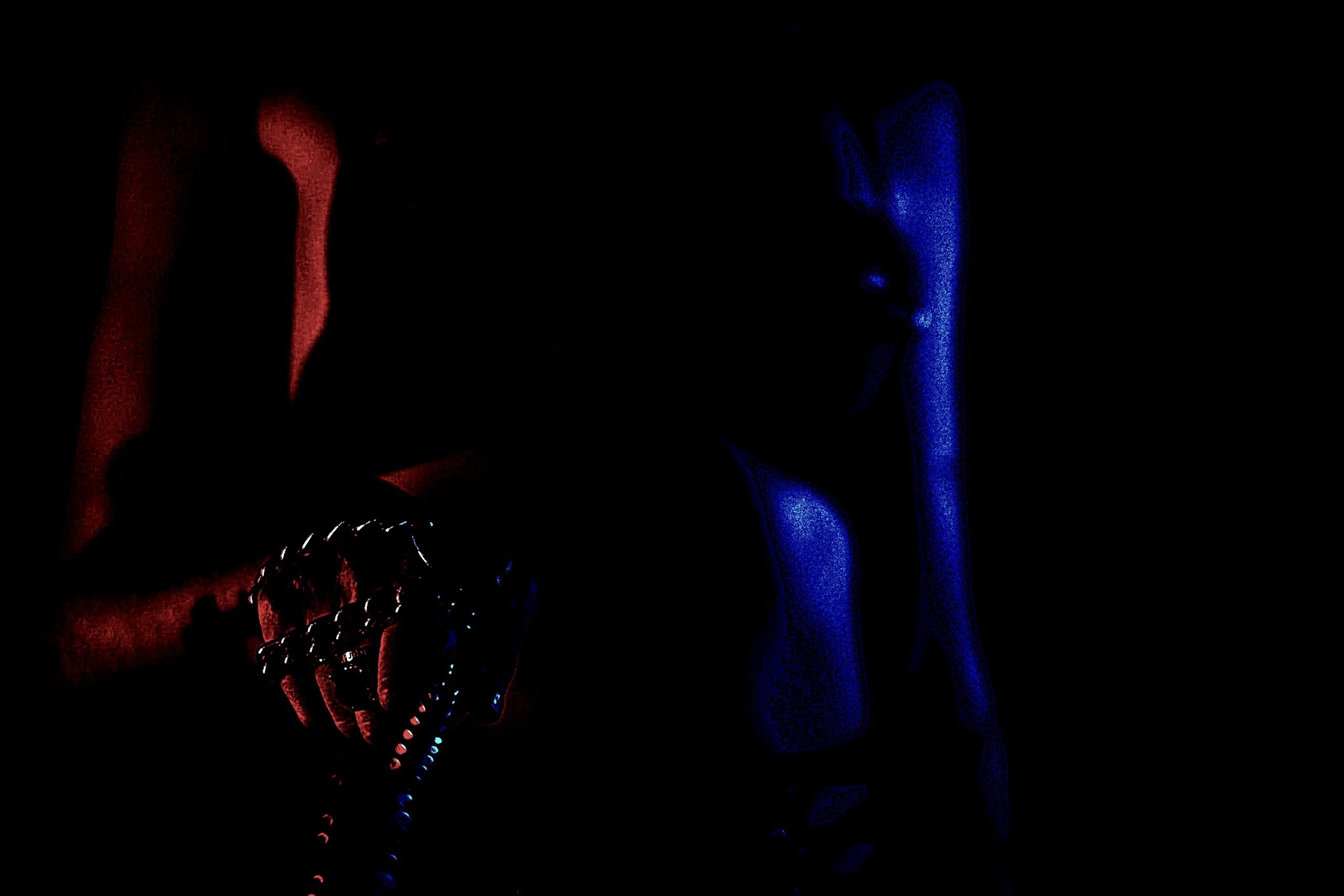 Person in fetish gear holding a riding crop, illuminated by red and blue light in a dark setting