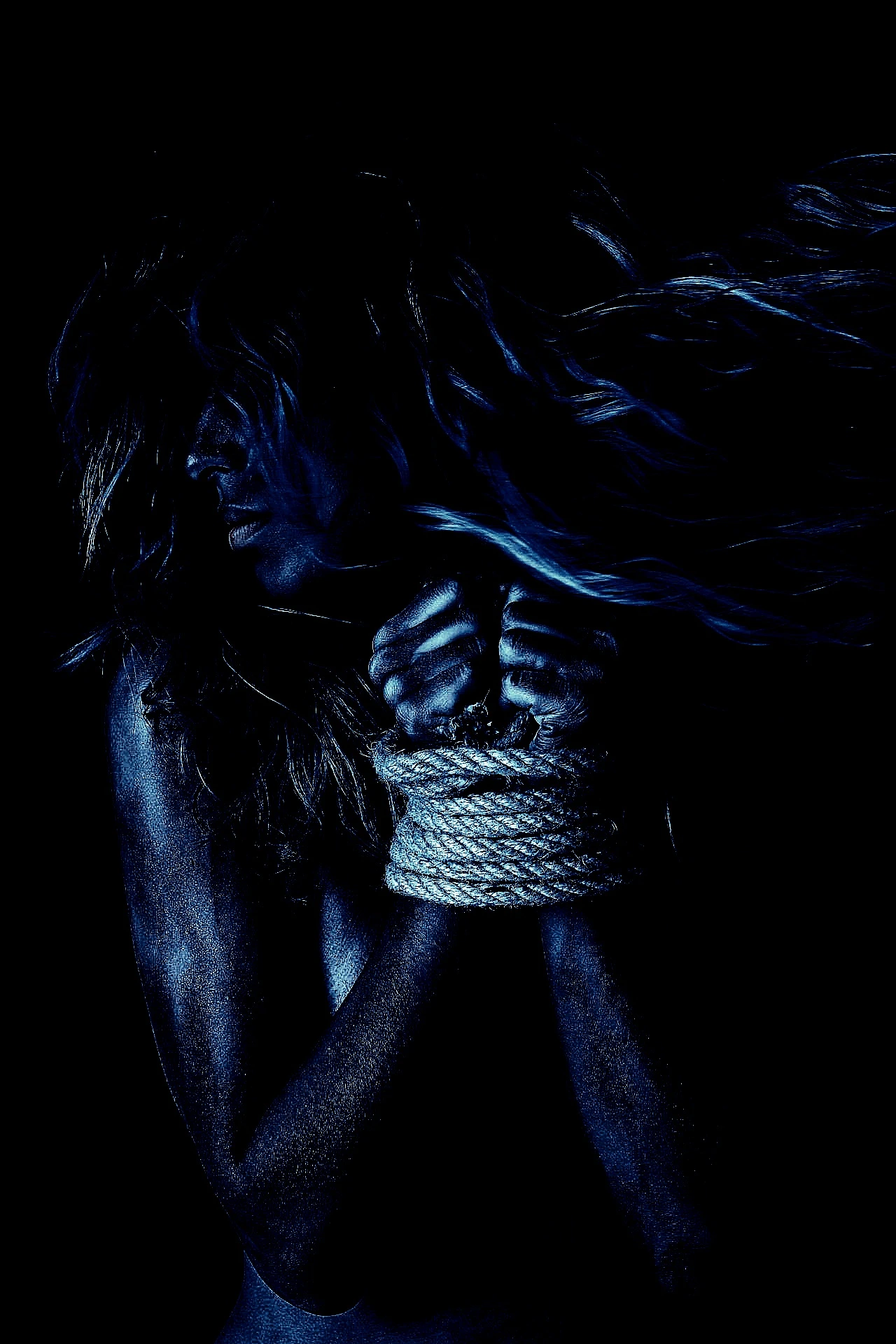 Woman with hands bound in rope, body painted blue, hair flowing in dramatic low light