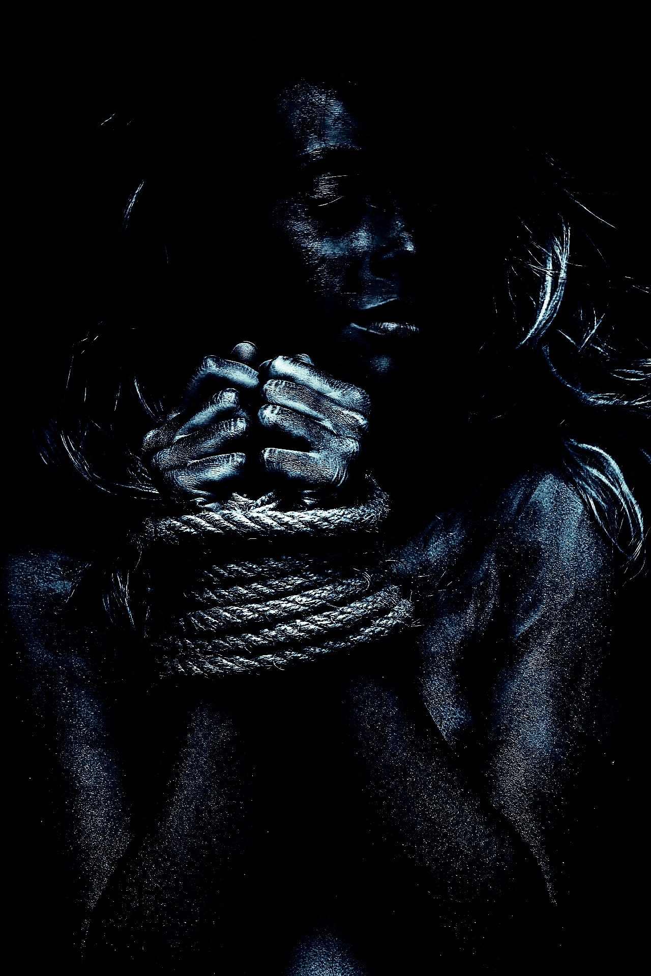 Artistic portrait of a bound woman in blue body paint with tightly clenched hands