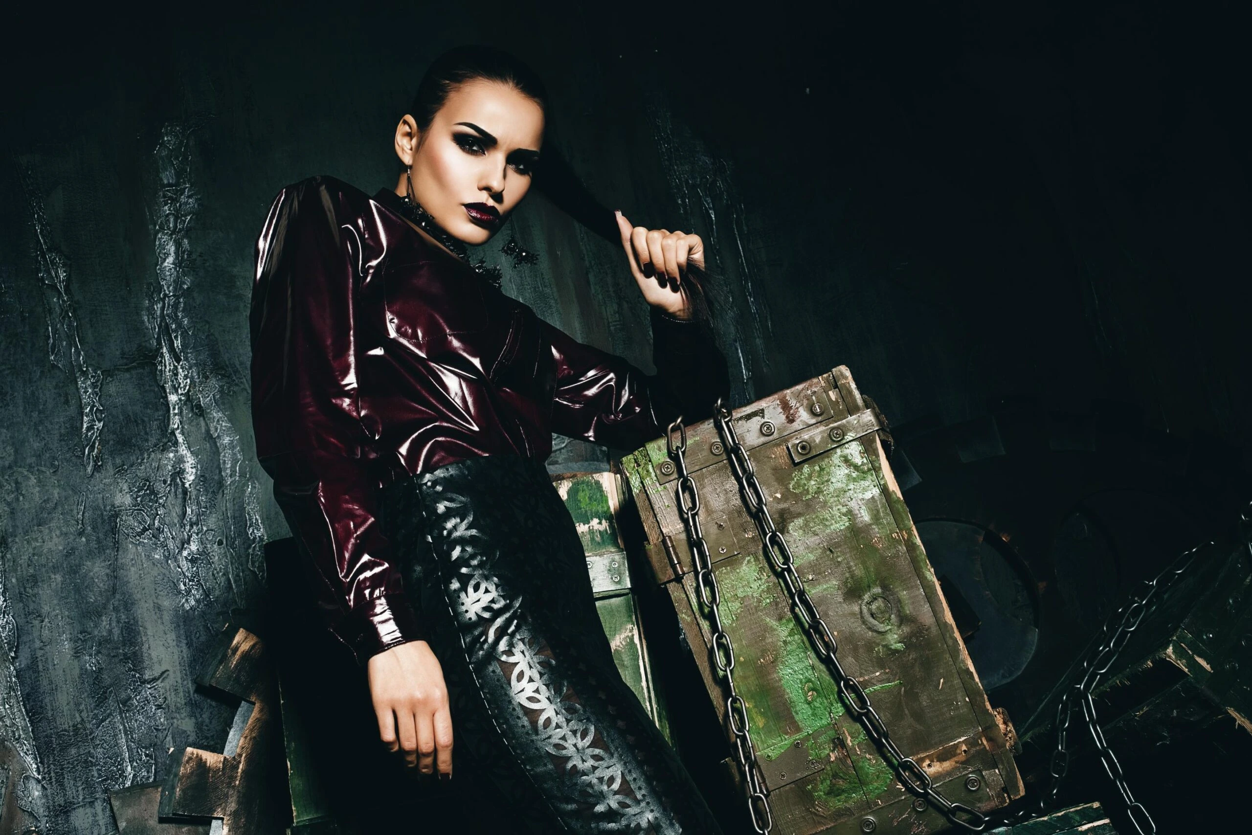 Gothic woman sitting on crates in black leather pencil skirt and burgundy vinyl shirt