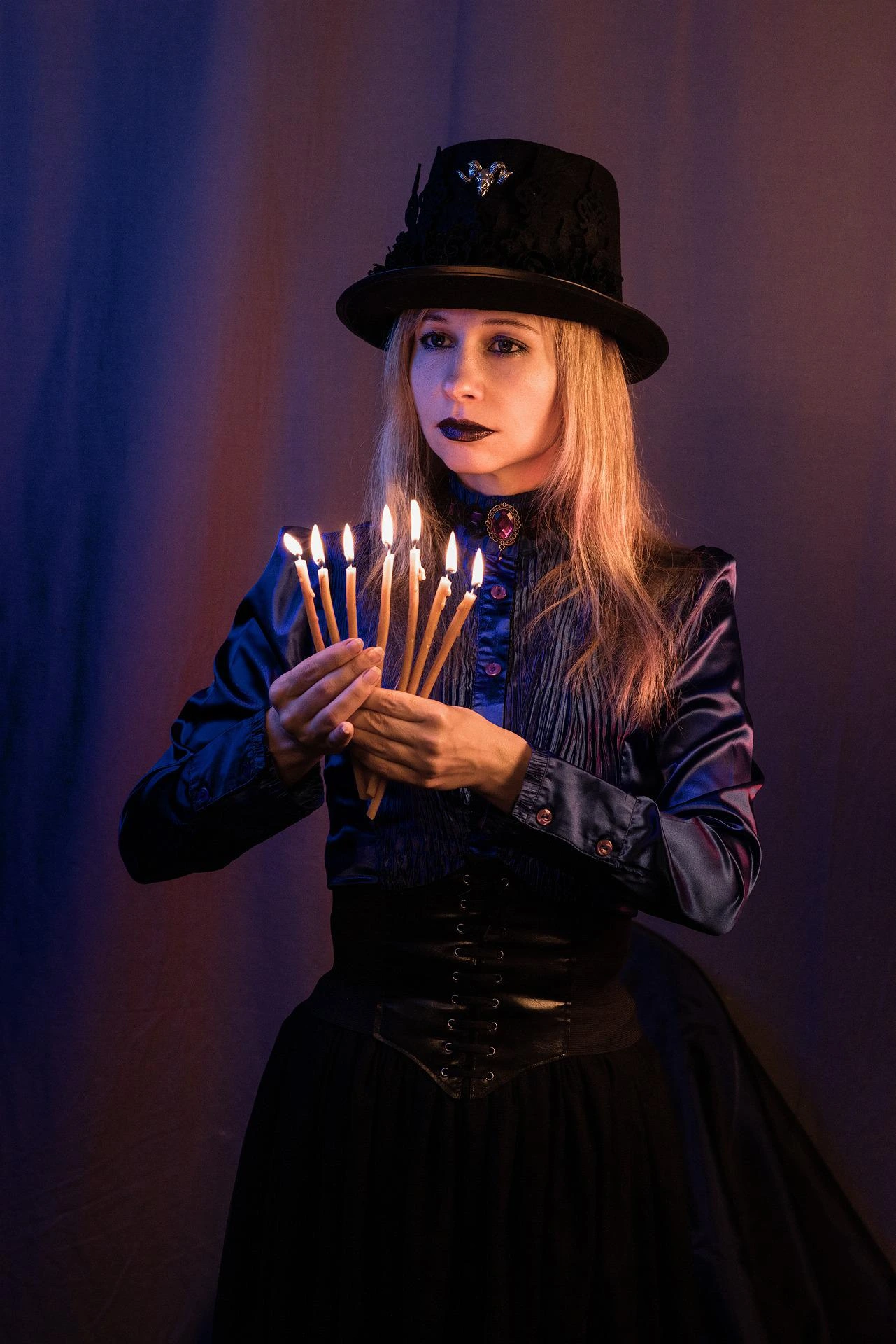 Red-haired woman in black strappy bodysuit holding two crystal balls in front of red-black drapes. 