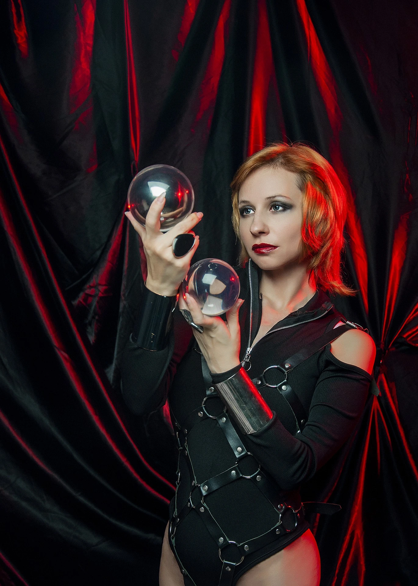 Blonde gothic woman in blue blouse and black corset holding lit candles, under moody low light. 