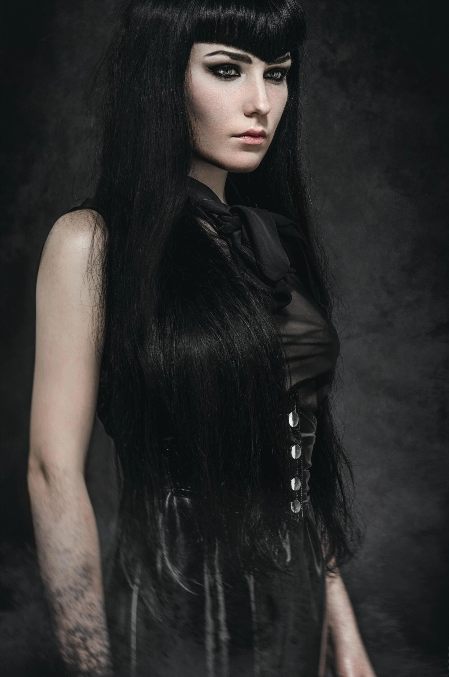 Gothic woman in black corset top and long hair, moody portrait with intense gaze.