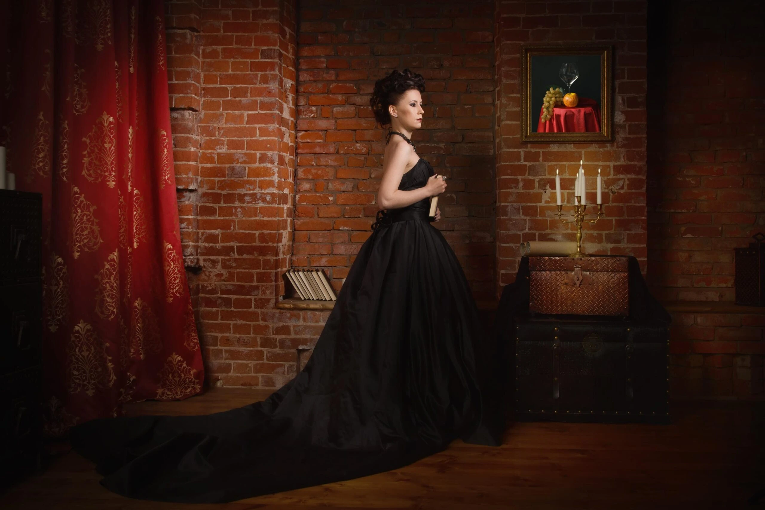 Woman in full-length black ball gown standing in gothic Victorian interior.