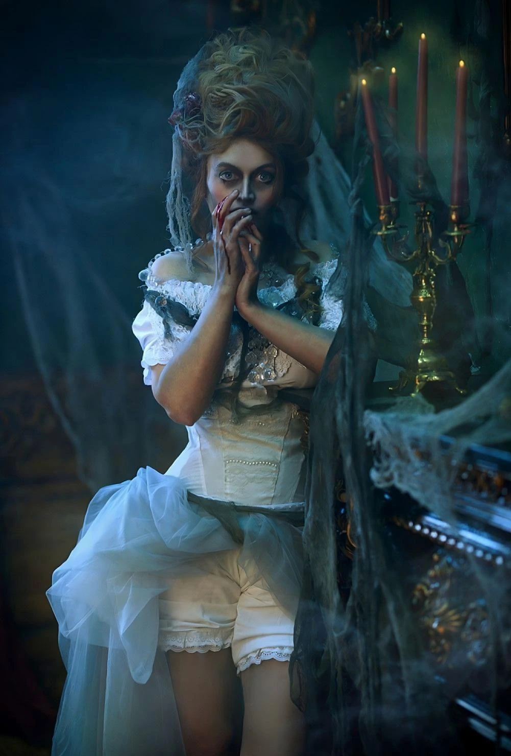 Haunted gothic bride in white corset dress with blood on fingers, standing in candlelit Victorian room with cobwebs.