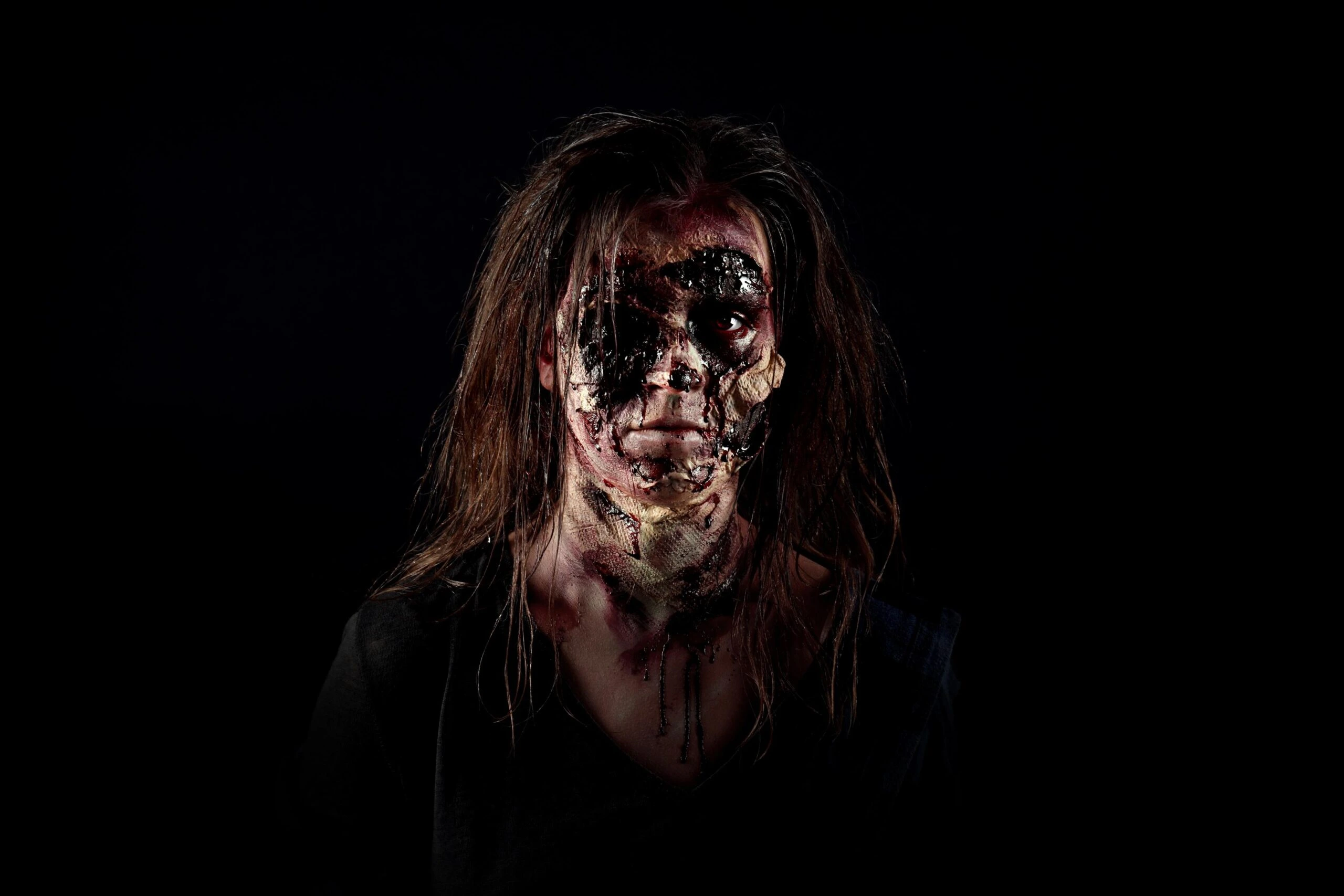 Horror-style woman with melted face makeup and long hair staring into darkness with haunting expression.
