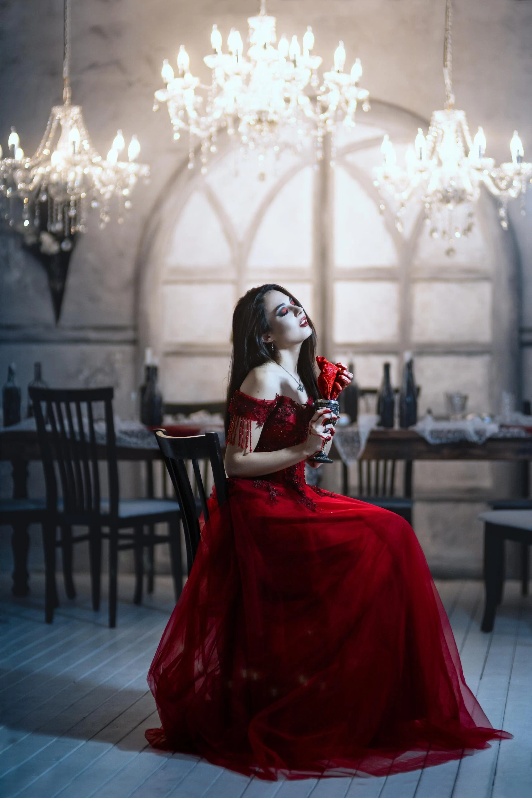 Vampiric woman in red gothic gown holding blood-covered roses, surrounded by chandeliers and a Victorian-style feast hall.