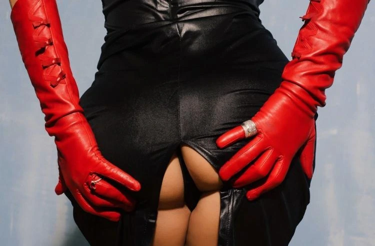 Woman in tight black latex dress and red leather gloves, suggestive pose with fetish elegance.