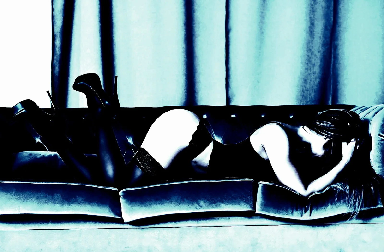 Artistic photo of woman in lingerie lying face down on a couch, edited in blue monochrome tones.
