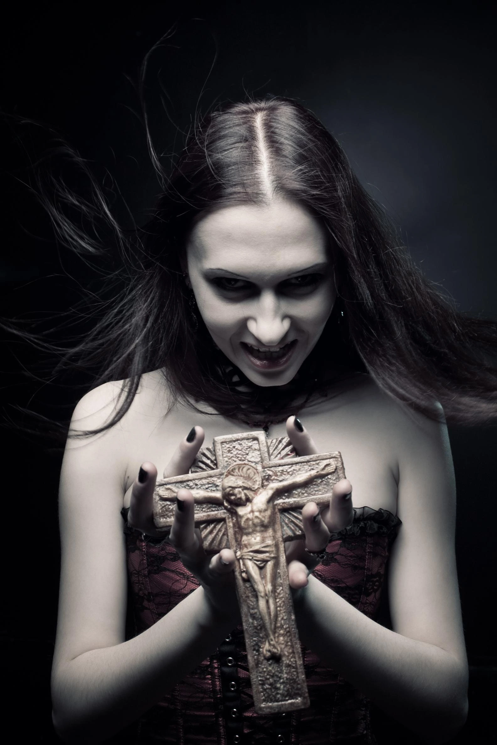 Gothic woman with long dark hair in a red corset, holding a large crucifix with a sinister expression. 