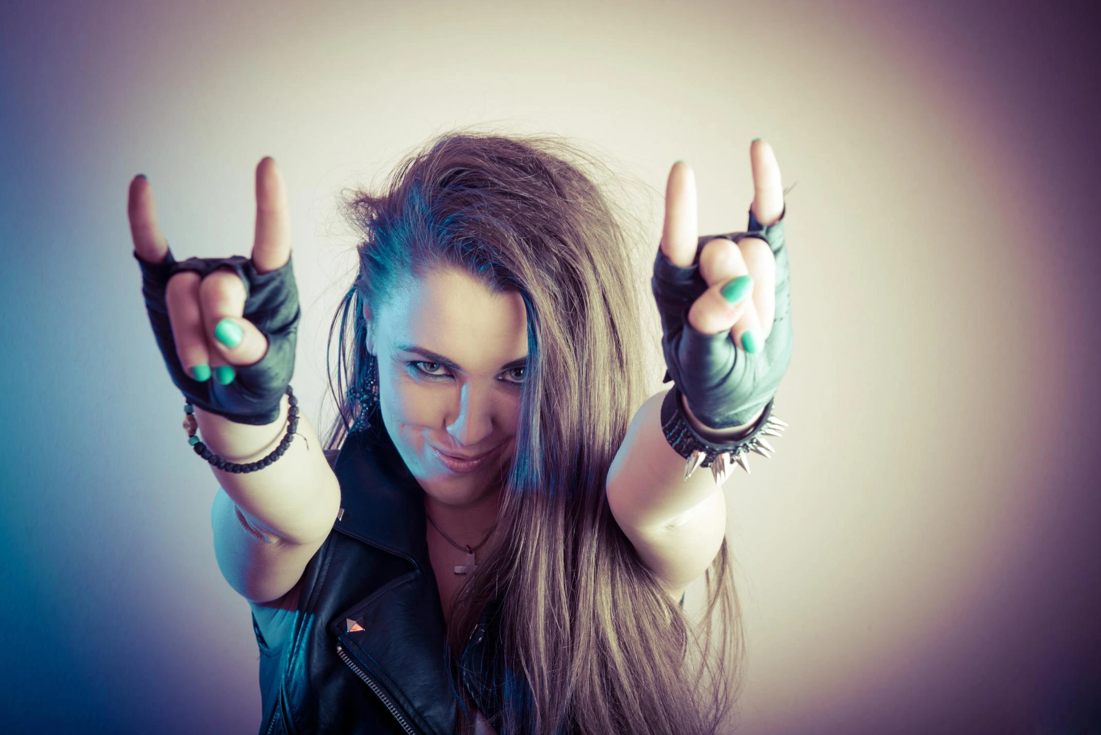 Metalhead woman smiling with leather vest and spiked bracelet making devil horns hand sign