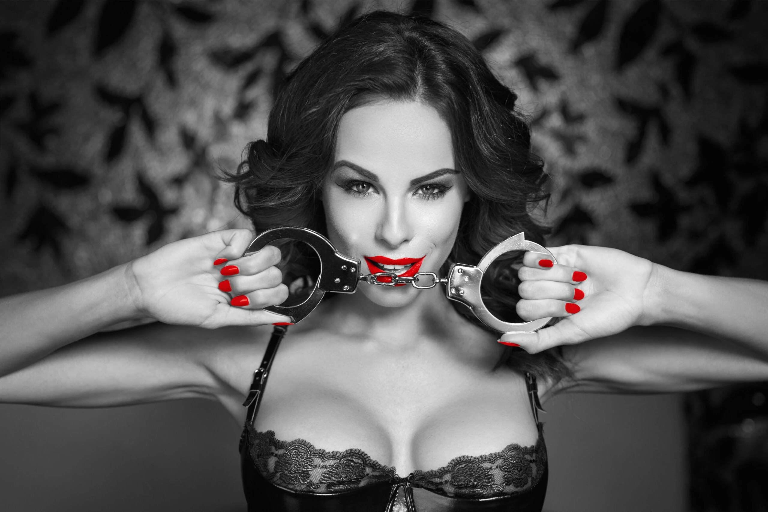 Black and white portrait of woman with red lips and nails holding handcuffs