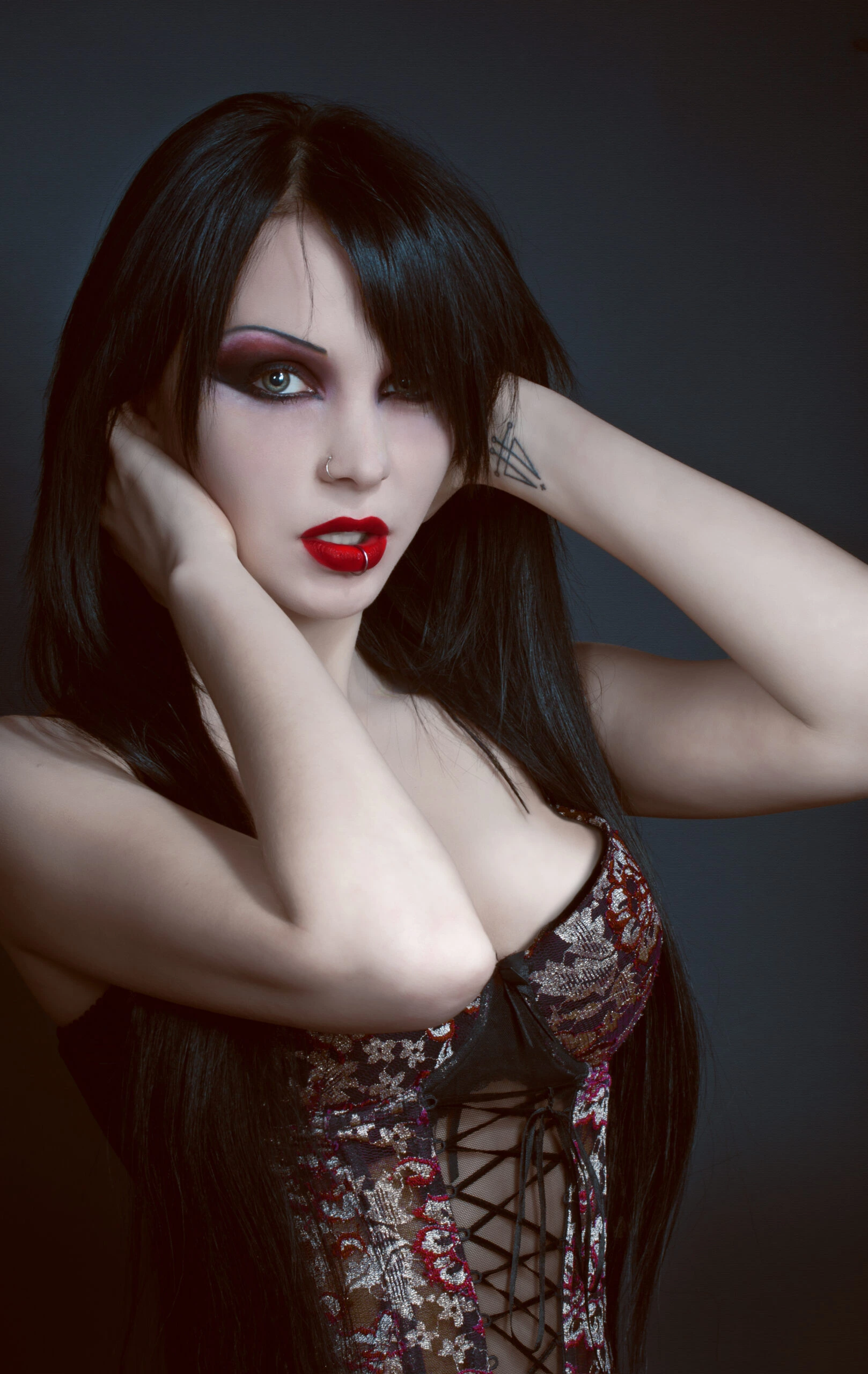 Goth woman with black hair, red lips, and smoky eye makeup holding her head with her hands.