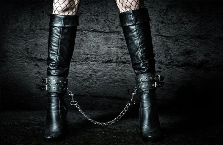 Close-up of black leather boots chained together with fishnet stockings on a gritty black floor