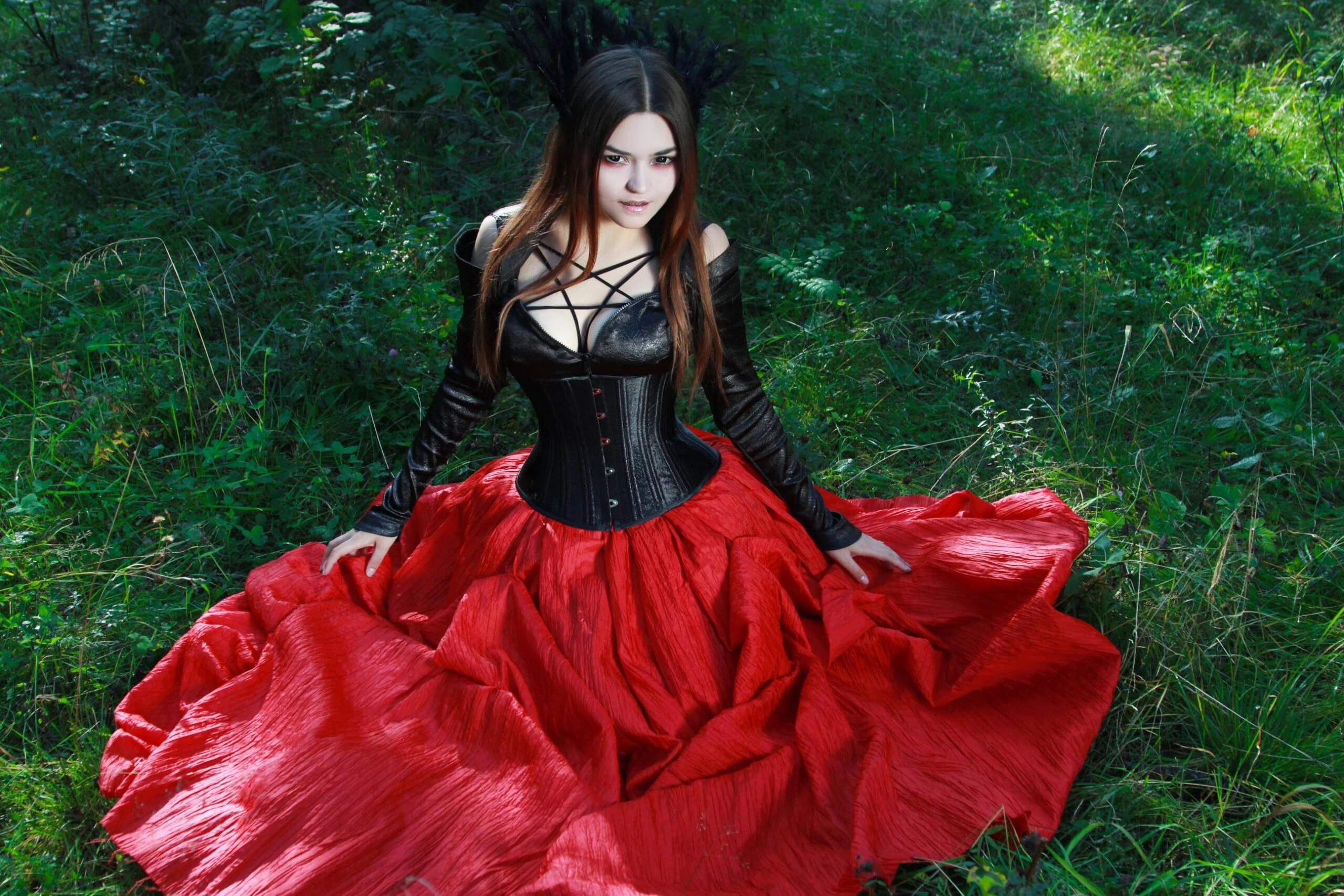 Gothic woman in a black corset and red skirt posing in a forest clearing.