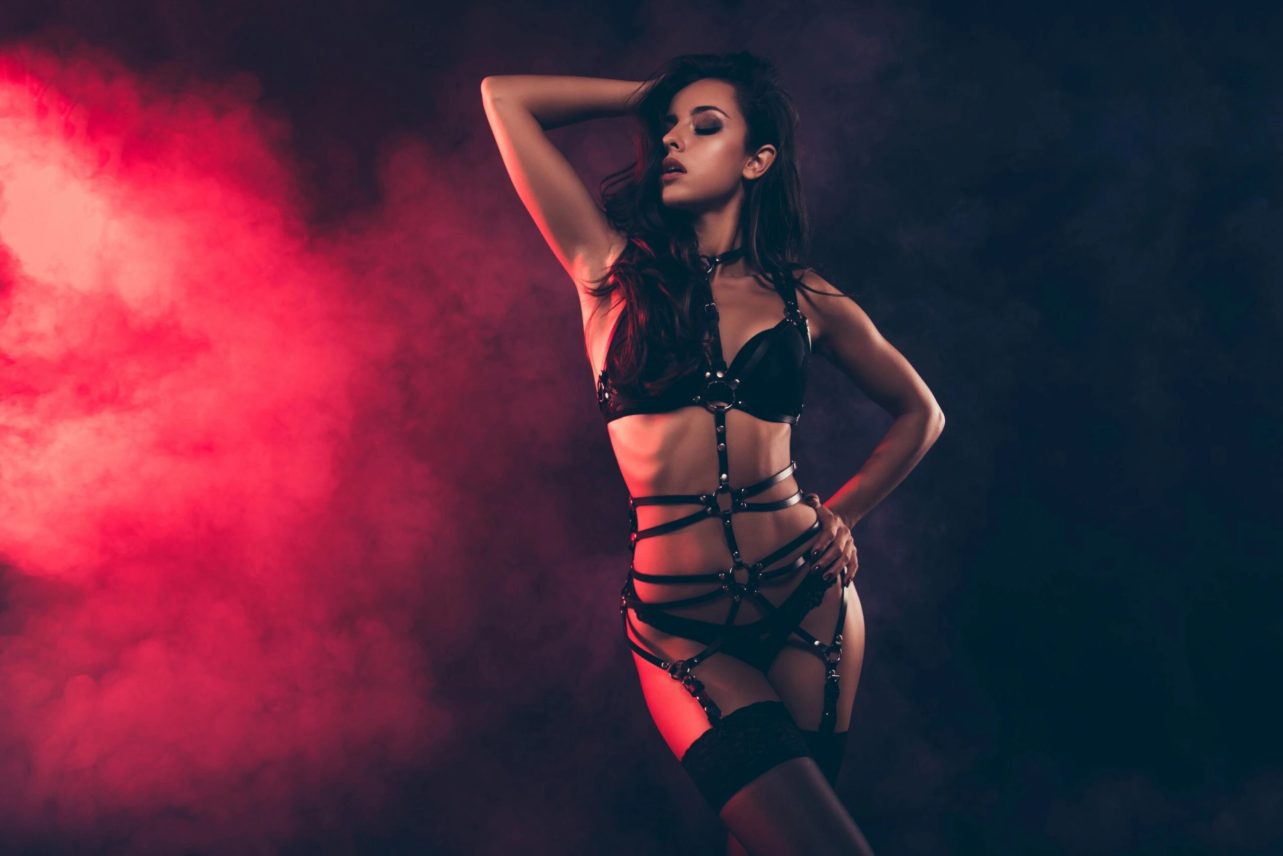 Studio portrait of a woman in a black corset-style harness, highlighting waist definition and fashion-forward design
