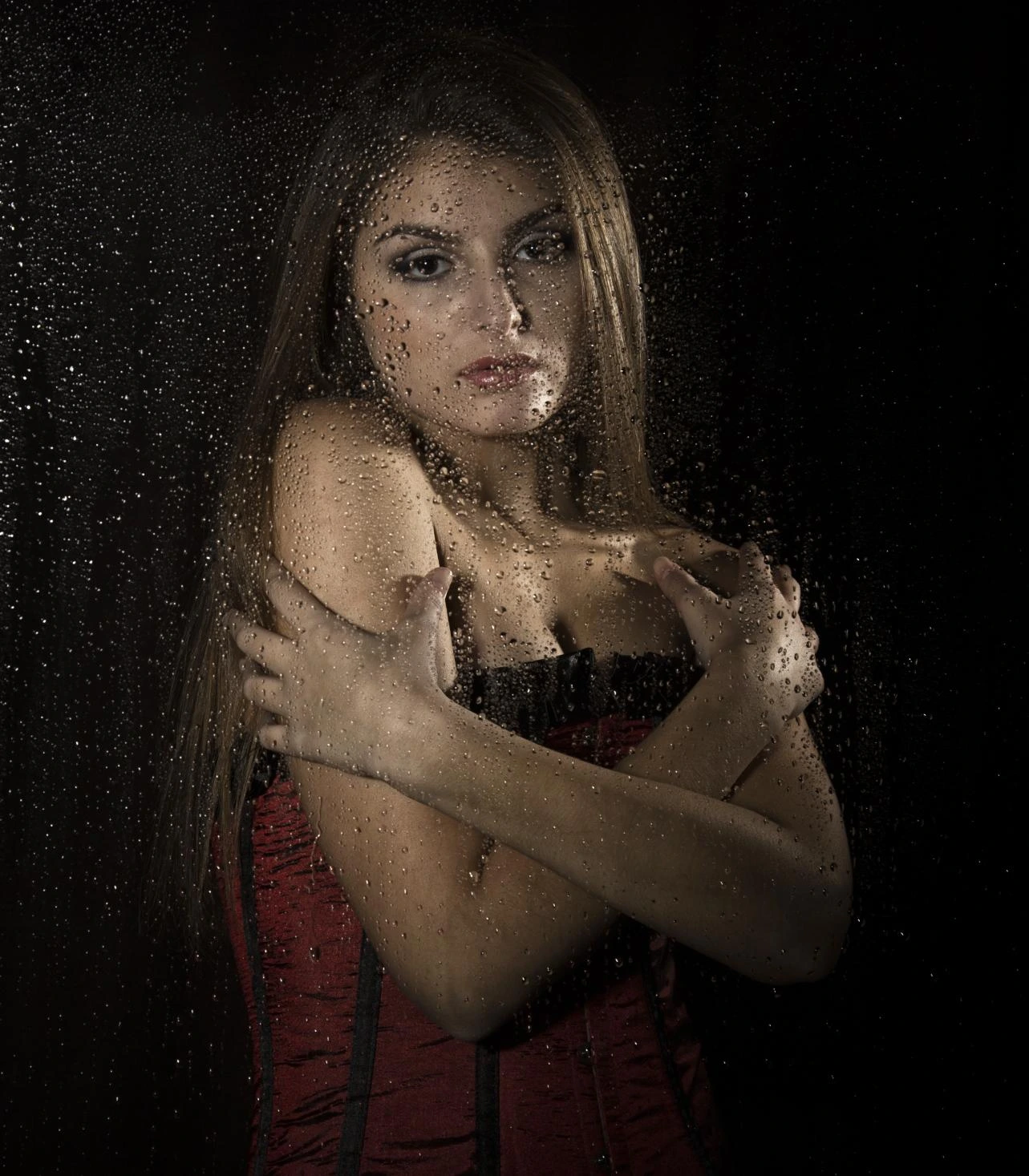 Moody portrait of woman behind rain-covered glass, bare shoulders crossed, soft light, dark background, emotional and cinematic tone.