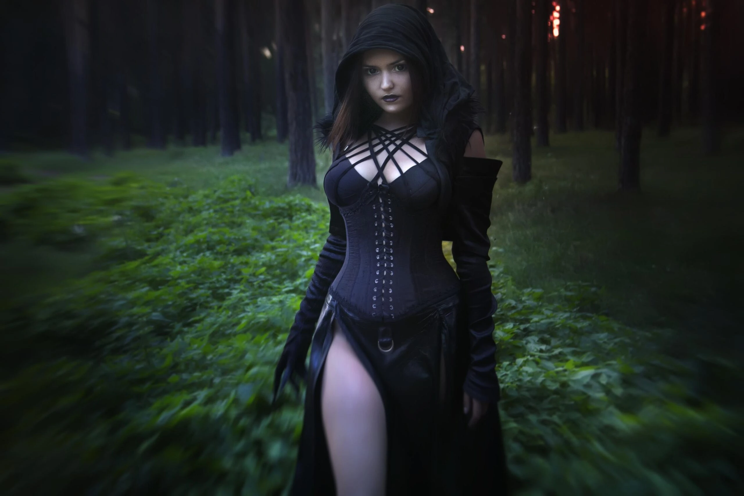 Woman in a dark hooded gothic outfit standing in a forest clearing, dramatic lighting and moody atmosphere.