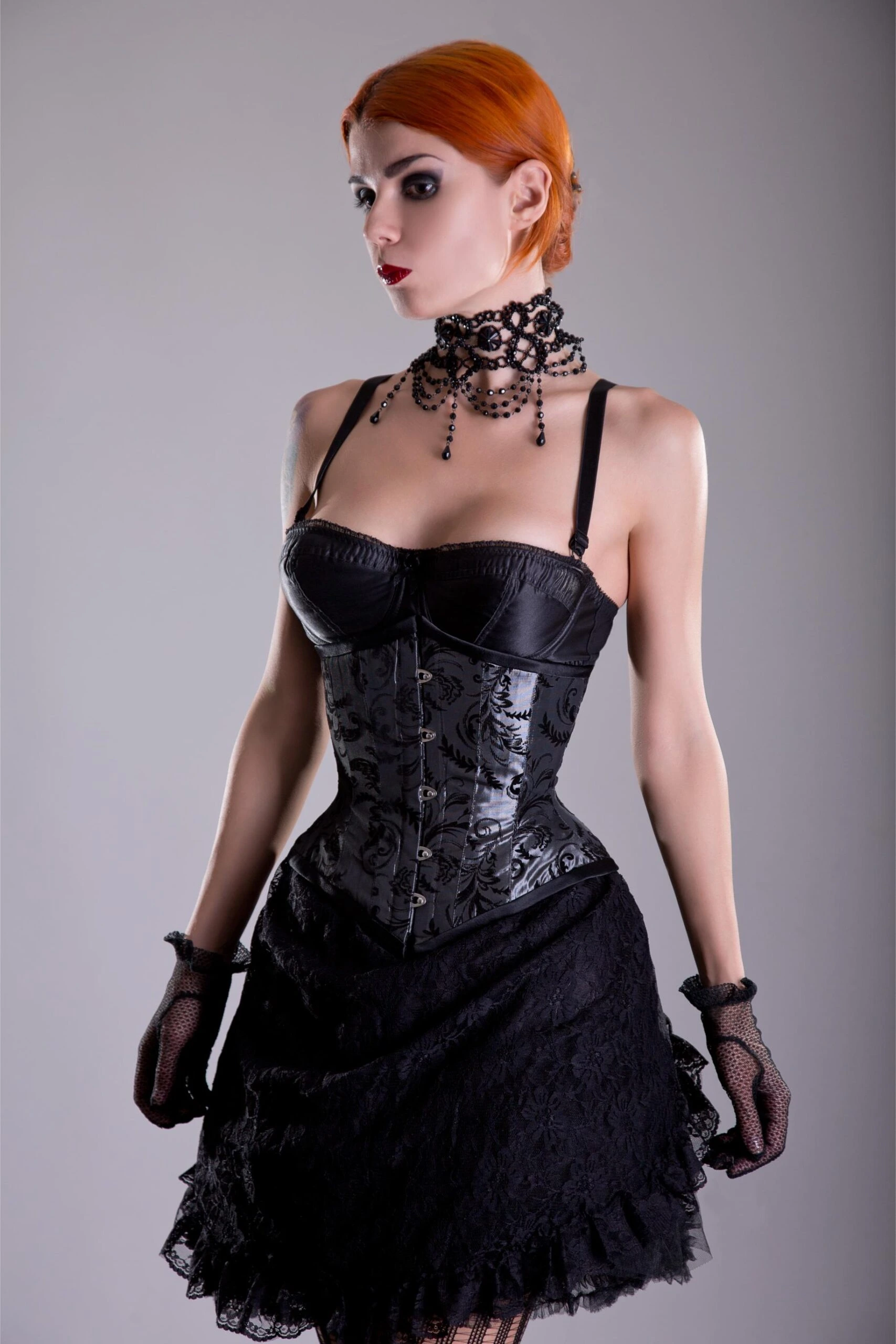 Woman with short orange hair wearing black corset and lace skirt with gothic choker.