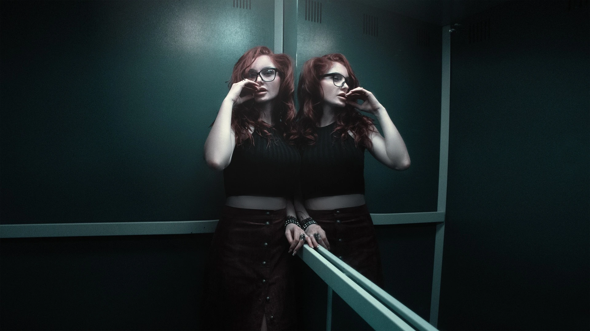 Red-haired woman with glasses standing in elevator beside mirror reflection.